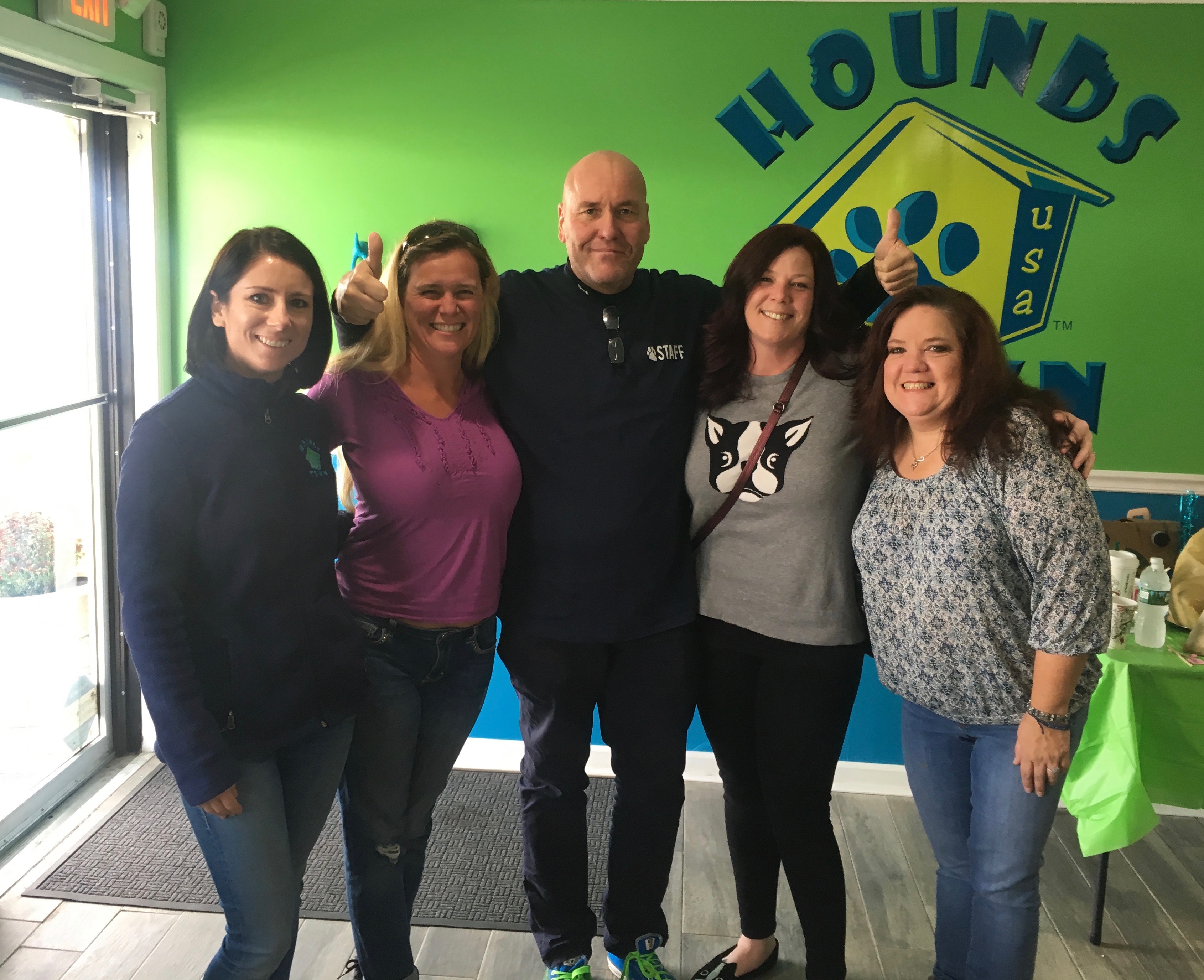 five people smiling in front of hounds town logo