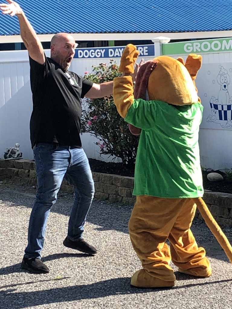 a man dancing with a person in a dog costume in a parking lot